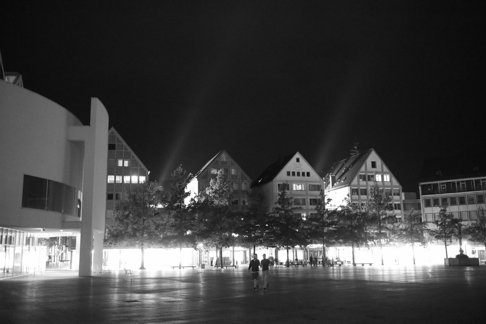b/w pic of houses at night with lights streaming upwards