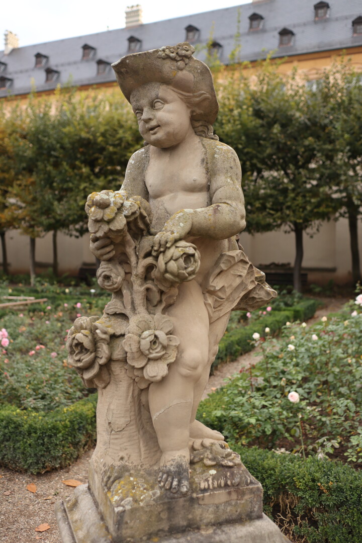 statue of some baroque angel-type figure with a hat in a park