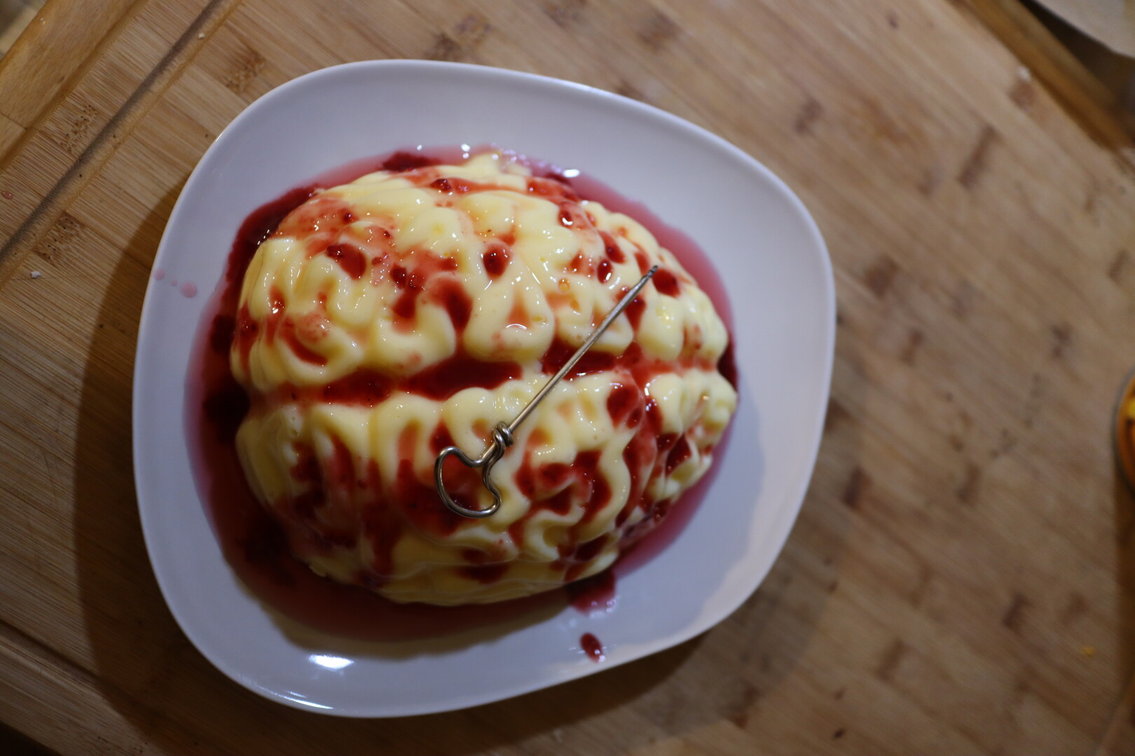 vanilla pudding in the shape of a brain with red syrup poured over. A drill placed across it